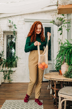 Smiling woman with reusable string bag of tangerines in garden