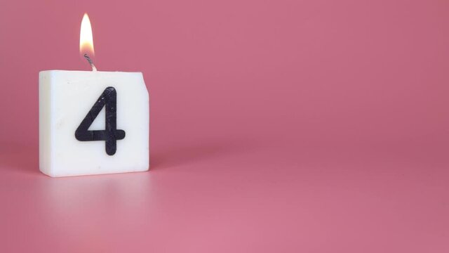 A square candle saying the number 4 being lit and blown out on a pink background celebrating a birthday or anniversary