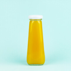 Yellow smoothie or juice bottle on blue background. Orange juice glass bottle.