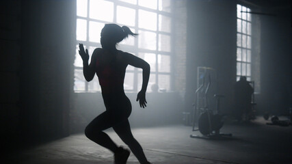 Fototapeta na wymiar Active sportswoman jogging in dark loft building. Strong woman running in gym