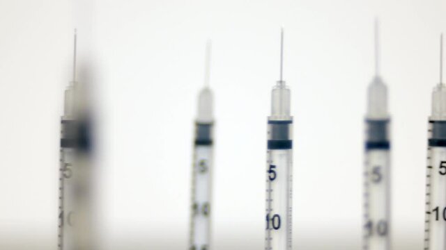 Empty vaccine syringes and medical needles standing upright on a table slow pan slide dolly