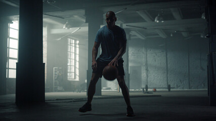 Fototapeta na wymiar Man having basketball training in loft building. Player bouncing basketball ball