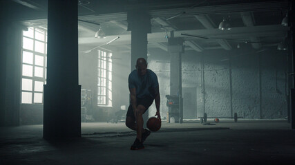 Fototapeta na wymiar Basketball player training in sport club. Sporty man dribbling ball between legs