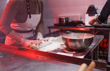 the girl cook rolls out the dough on a metal table in the kitchen in a restaurant. beautiful lighting. close-up.