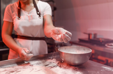 a female cook sprinkles flour on a metal table in the kitchen before making dough. close-up