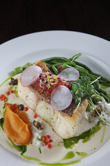 Pike perch with white sauce and beans. A white plate. Menu for the restaurant. Healthy and low-calorie food. A dish of fish with beans. Close-up.