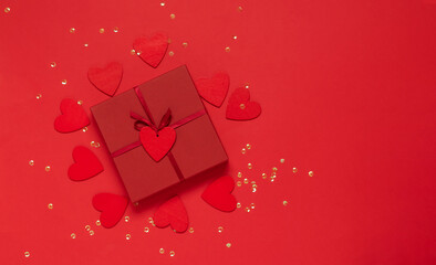 Gift with a red bow on a red background with glitter hearts and confetti. Festive flat composition for Valentine's Day, New Year, Mother's Day, Wedding. Mockup with copy space