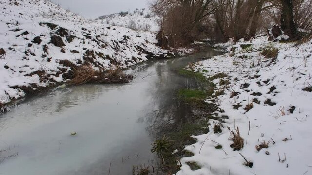 Winter river. Dirty water enters the river channel through a pipe. Sandy bottom.