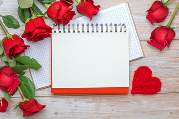 Opened hardback plaid notebook, heart-shaped gift box with satin bow, roses and petals, string valentine, wooden surface. 14 february, Engagement, wedding anniversary, romantic evening planning.