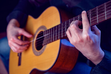 Fototapeta premium The guy in the dark shirt is plucking the strings of a six-string guitar