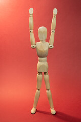 Wooden mannequin holding arms above the head, doing sport exercises, picture on red background
