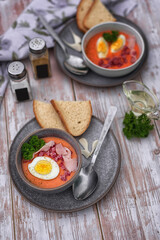 Cold tomato soup or gazpacho. Cold Spanish salmorejo soup made of tomatoes, bread, garlic and olive oil. Serving in a gray ceramic dish on a light wooden background. Summer cold vegan food/
