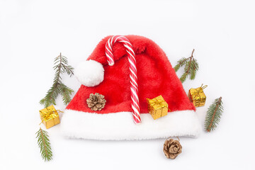 Fir branch, cones, caramel cane, gift, in the hat of Santa Claus on white background