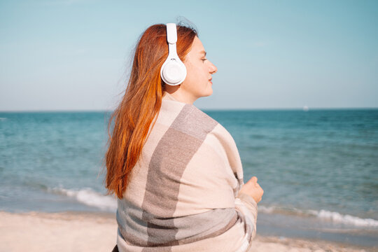 Image of thinking dreaming caucasian cheerful ginger woman meditating listening to smartphone music phone app on beach. Side view