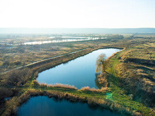 Top down aerial view with early spring meadows, pond and river. 