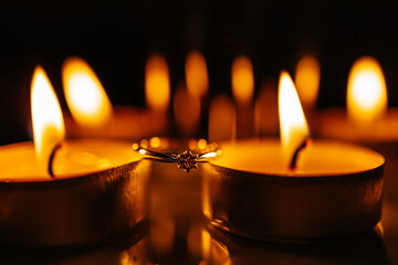 an engagement ring between the burning candles with fire bokeh background