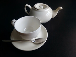 White cup and saucer and teapot isolated on black background
