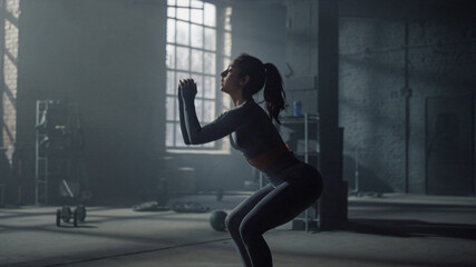 Woman in sportswear doing squats in crossfit gym. Girl making squats with jumps