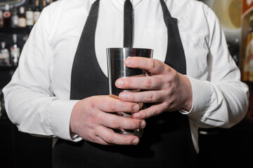 The hands of a professional bartender man holds a tool for mixing and making shaker cocktails