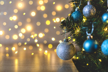 Decorated Christmas tree with silver, blue shiny and frosted balls on a background of orange sparkling fabulous blurry lights, empty space on a brown wooden table. New year card concept, close-up