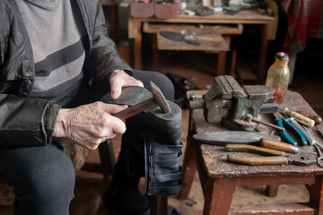 A retired shoemaker repairs shoes. There are many instruments near it.