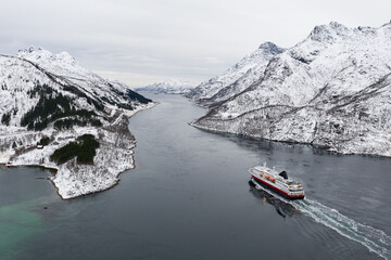 Aerial view of fjord in cold winter weather with Hurtigruten ferry turist boat on the sea. Lofoten near Trollfjorden. Panoramatic photography in foggy weather.