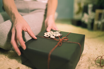 Woman decorating xmas gift box wrapped on background of Christmas tree and lights. Presents preparation on winter holidays