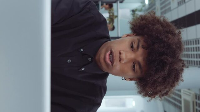 Vertical Screen: African American employee using laptop in office and mumbling something, diverse coworkers on background. Arc shot man working online, browsing internet. Concept of business