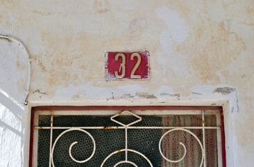 Window with Iron Security Grill and Painted Number 32 on Wall of Old Building with Flaking Paint 