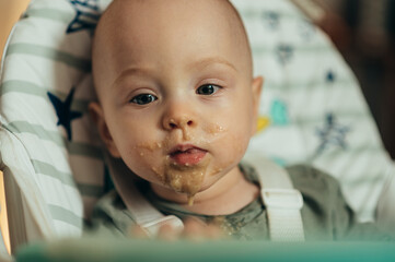 Baby eating with a face stained in food while in a child's dining chair