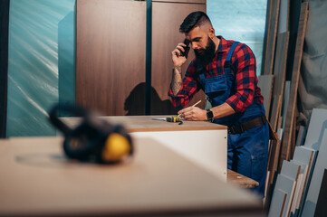 Young male carpenter working in workshop and using smartphone