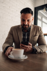 Businessman using smartphone while drinking coffee in a cafe