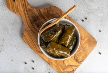 Stuffed grape leaves in olive oil in a bowl on the olive wood cutting board, photographed from above