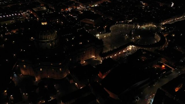 Aerial drone night video of illuminated Saint Peter's square, world's largest church - Basilica of St. Peter's, Vatican - an elliptical esplanade created in the mid seventeenth century, Rome, Italy