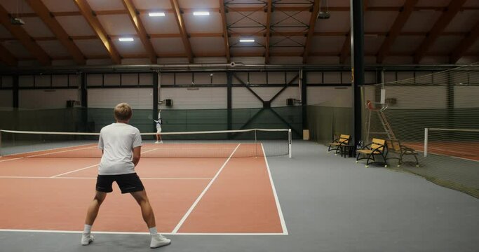 Paired tennis game between a young man and a woman in an indoor tennis court