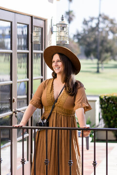 Smiling woman wearing brown dress & hipster hat looking into distance