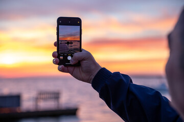 Man taking photo with smartphone of beautiful ocean sunset.
