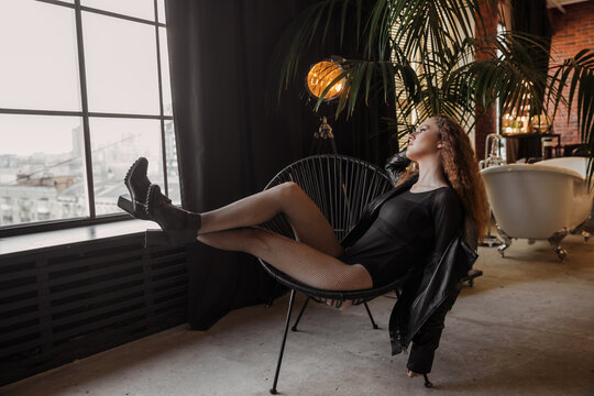 Cheerful amazing red haired curly girl in a black leather jacket sitting on the chair