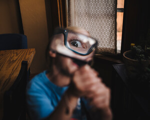 Caucasian little girl holding magnifying glass up to eye indoors