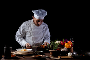 Male chef in white uniform prepares spaghetti with vegetables on the dish
