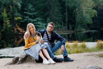 A man with a woman and a dog are sitting in nature. Papillon for a walk in the forest with the owners.