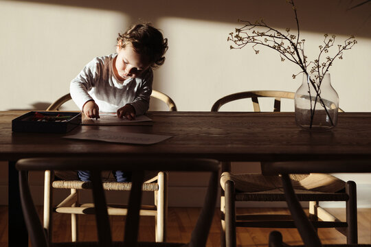 Little kid drawing at home alone lit by the sunrise