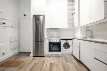 White kitchen with white countertop and large white cabinets and fitted appliances in a vacation rental apartment