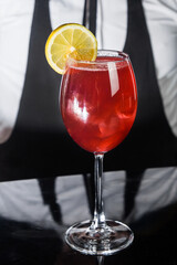 Red alcoholic beverage cocktail in glass decorated with a slice of lemon on the bar counter against the background of the bartender