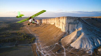 A light-engine plane is flying over a white rocky mountain. Shooting from a drone.