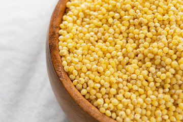 Wooden bowl with uncooked millet on a white crumpled napkin. Macro