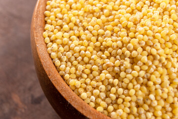 Full rustic wooden bowl with dry millet on a wooden table. Macro