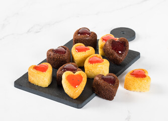 Small holiday vanilla and chocolate cakes cookies in the shape of a heart with strawberry marmalade filling on a serving board on a white background. Valentine's Day