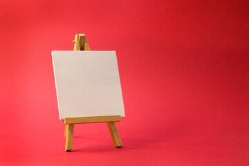 Easel for artists miniature on bright red background. Art minimal concept.