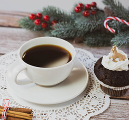Obraz na płótnie Canvas A white cup with black coffee, chocolate muffin and other Christmas decorations are on a light wooden table. Square image. 
